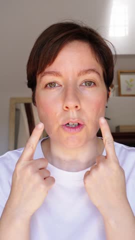 Middle aged woman performs a facial yoga exercise focused on the lower eyelid muscles to tone and rejuvenate the eye area. Filmed vertically in bright home, tutorial style content for social media. 4K