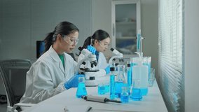 Female scientific researchers collaborating, analyzing experimental data through microscope and glassware while discussing research findings in modern laboratory setting - Powered by Shutterstock - Get 15% off with code: PIKWIZARD15