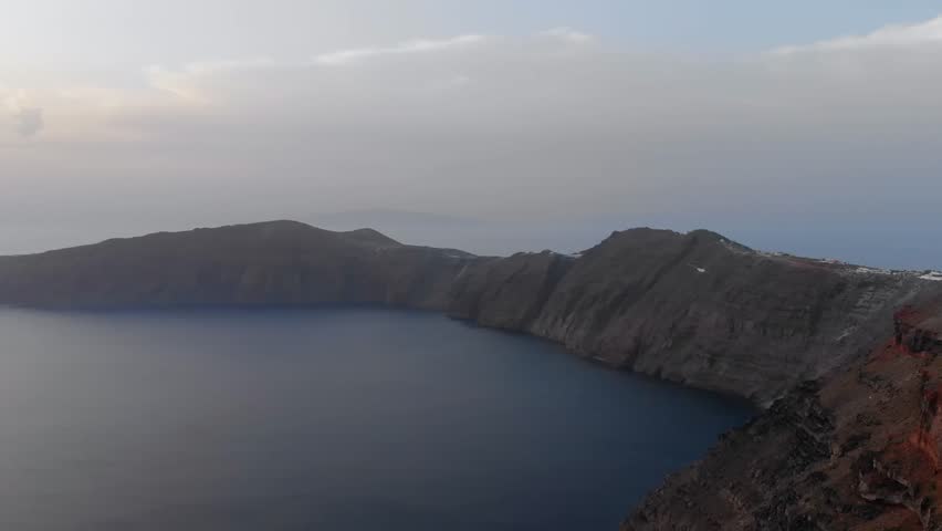 panoramic footage capturing the iconic caldera of Santorini, Greece. The dramatic cliffs, formed by ancient volcanic activity, plunge into the deep blue waters of the Aegean Sea, showcasing the island
