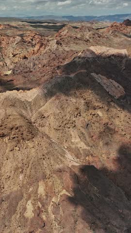 Aerial view reveals the expansive desert terrain of Nevada, characterized by rugged mountains and shadowed valleys under a clear sky.