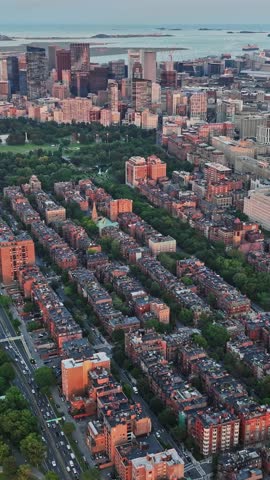 Looking down on Boston, urban buildings rise alongside lush parks and waterways, illustrating the dynamic blend of city life and nature in this historic location.