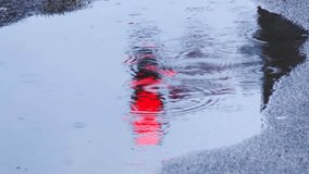 Raindrops creating rhythmic ripples across puddle surface, mirroring urban landscape with red traffic light and shadowy silhouette on wet asphalt road during rainy daytime - Powered by Shutterstock - Get 15% off with code: PIKWIZARD15