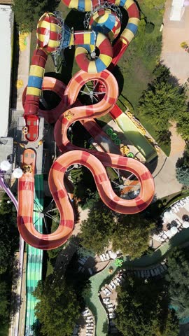 Aerial view of colorful twisting water slides with people riding inflatable tubes at a water park. Bright summer day filled with thrill, fun, and excitement