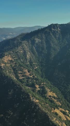 This aerial perspective captures the breathtaking California mountains with deep valleys and verdant landscapes under a clear blue sky. The view highlights natural beauty.