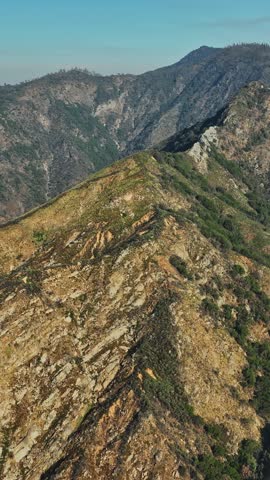 An aerial perspective reveals a stunning mountain range in California, featuring rocky ridges and lush vegetation under a clear blue sky.