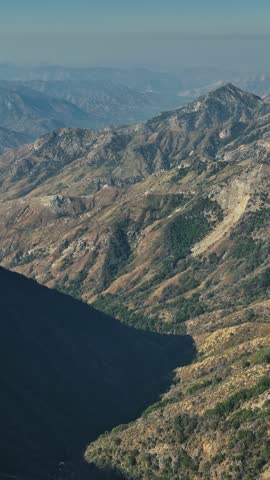 Vast mountain ranges stretch endlessly across California, showcasing a blend of rugged terrain and vibrant vegetation under clear skies and bright sunlight.