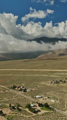 Expansive aerial view captures the arid Nevada landscape, showcasing scattered homes, fields, and dramatic clouds looming over distant mountain ranges.