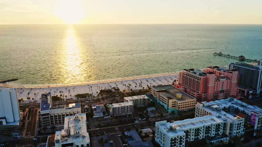 The sun sets over the Gulf of Mexico, casting golden reflections across the water as Clearwater Beach hotels and pier frame this iconic coastal vacation scene.
