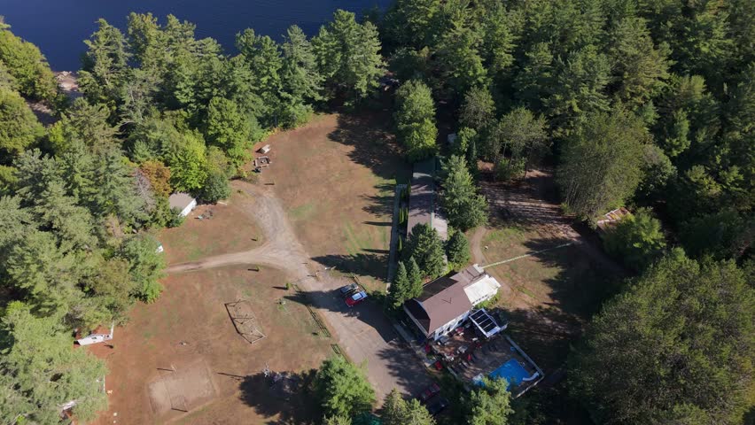 Drone top-down shot over forest houses in Muskoka showing green trees, open ground, cottages and a water body with small cascade at High Falls.