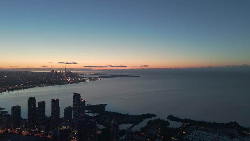 Drone aerial shot at sunrise showing Parklawn neighbourhood with residential towers, Lake Ontario shoreline, and Toronto downtown skyline in the background.