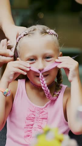 Beautiful blond girl, of seven years old, braided two pigtails, do a hairstyle with pink locks of hair in a beauty salon, a hairdresser