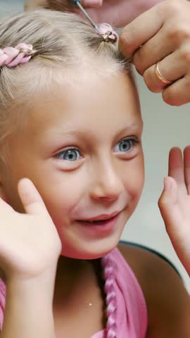 Beautiful blond girl, of seven years old, braided two pigtails, do a hairstyle with pink locks of hair in a beauty salon, a hairdresser