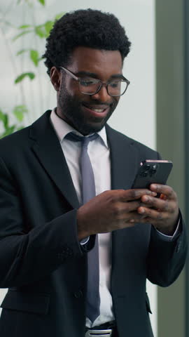 Smiling African American businessman using smartphone in office business man ethnic male guy looking at mobile phone cheerful professional entrepreneur checking messages browsing internet success