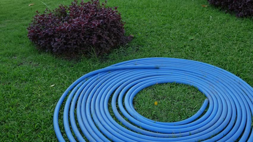 Blue Water Hose Coiled in Spiral Pattern on Green Grass Lawn - Garden Equipment and Yard Work.