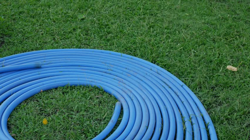 Blue Water Hose Coiled in Spiral Pattern on Green Grass Lawn - Garden Equipment and Yard Work.
