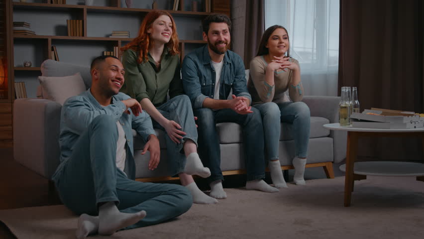 Four multiracial friends watching television tv laughing smiling carefree at home party discuss comedy funny movie cinema film multiethnic people watch modern smart tv humorous show women men together