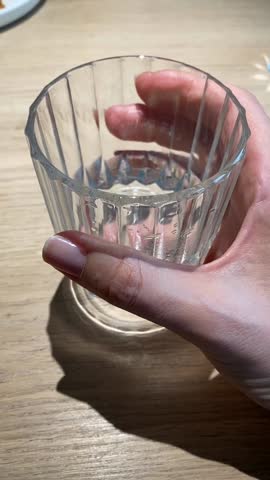 Hand holding empty glass on wooden table with sunlight casting shadow, suitable as background video