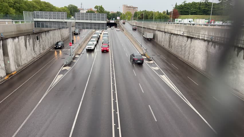 Verona, italy 10 september 2025: cars are driving on a multi-lane road next to a concrete barrier, leading to a tunnel entrance on a rainy day in verona, italy