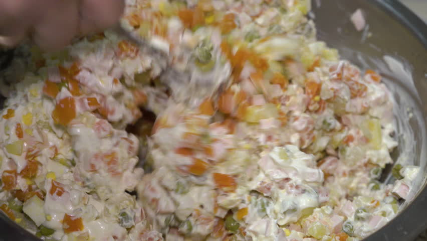 stir salad olivier with spoon, hand mix salad in a large bowl with potatoes, carrots, sausage and green peas