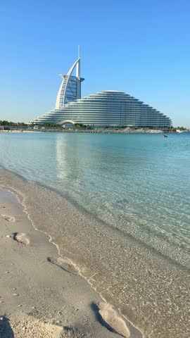 Burj Al Arab and Jumeirah Beach Hotel viewed from calm turquoise water in Dubai, UAE. A modern skyline featuring iconic architecture, resort luxury, and coastal elegance