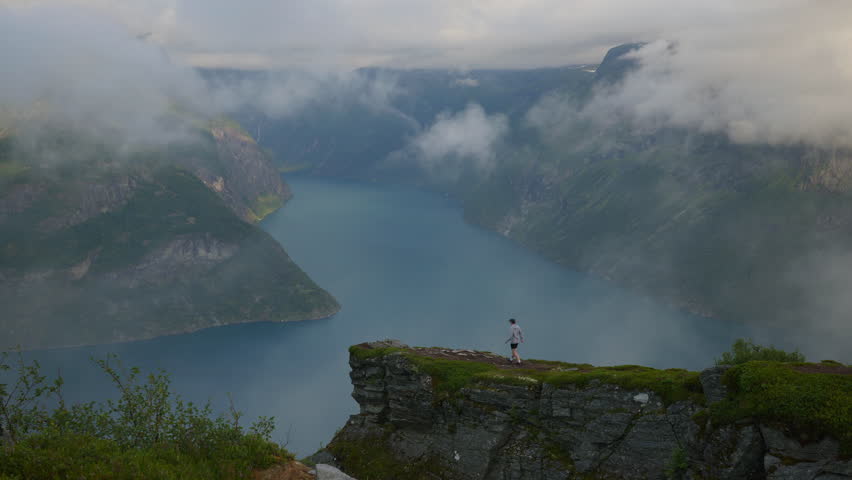Man walks to the cliff and looks out to the fjord enjoying the view