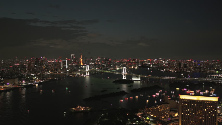 Twilight deepens over Tokyo Bay as Rainbow Bridge and Tokyo Tower anchor the frame. Traffic streams, boats glide, and the camera holds a steady cinematic panorama for tourism appeal