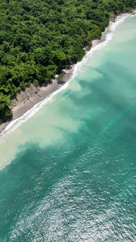 An aerial view of the turquoise waves hitting forest-lined shores in Reserva Natural Cabo Blanco, Costa Rica