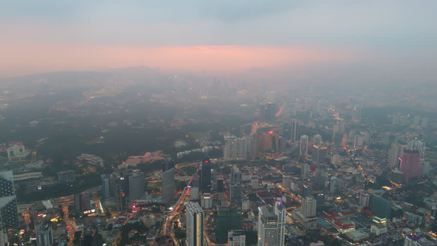 Panoramic climb at sunrise opens Kuala Lumpur across KLCC and Bukit Bintang as haze colors the horizon. Arteries of traffic wake below the parks, delivering a broad perspective for travel and economy