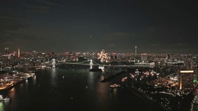 Aerial view sweeps across Tokyo Bay at night, revealing Rainbow Bridge and Odaiba Marine Park. Firework burst rises from Star Island, reflection shimmers on water, skyline glows with Tokyo Tower - Powered by Shutterstock - Get 15% off with code: PIKWIZARD15