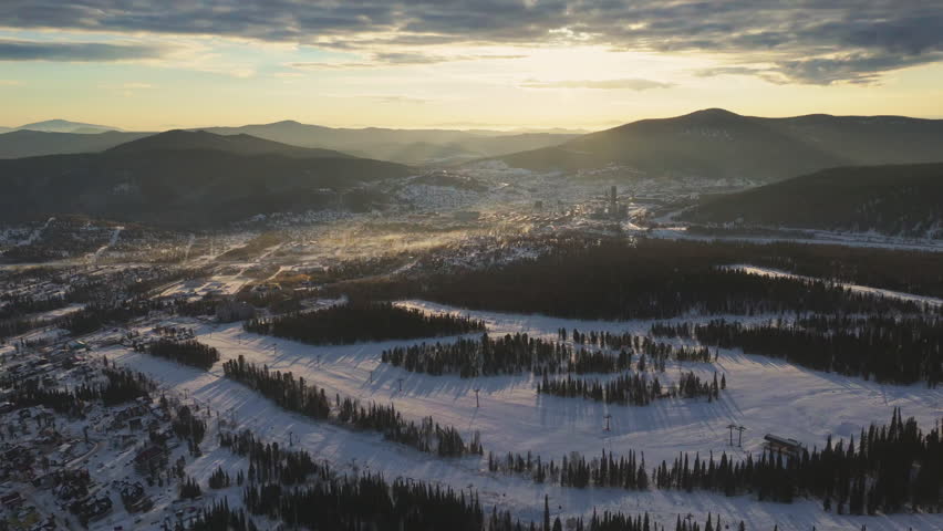 Golden morning light drifts over the Siberian town of Sheregesh and nearby mountains. Mist shimmers in the valley while long pine shadows stripe the snow, promising winter travel and resort adventure