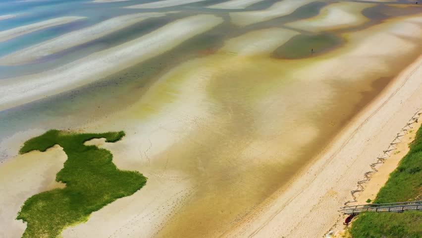 Drone footage capturing Cape Cod beach at low tide, where tidal pools glisten between sand ridges and dunes frame the coast, offering a cinematic and peaceful view of the Atlantic shoreline.