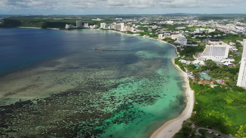 Panoramic view of stunning coastal reef and shoreline of Tumon Bay facing tropical island Guam with hotel resorts - aerial drone shot