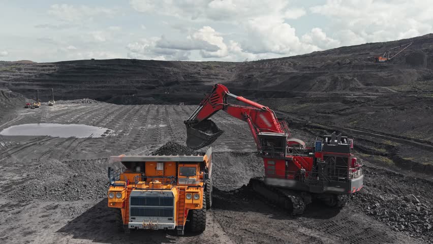 Aerial view process Industrial excavator loads coal into back of yellow heavy dump truck in open pit mine, concept mining industry.