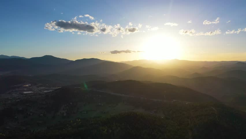 Sunset aerial panorama of Golden, Colorado, Table Mountain in deep orange light, foothills green and lush, and a highway weaving between the landscape with vehicles.