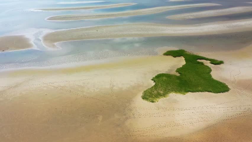 Aerial drone view over Cape Cod beach at low tide, showing rippled sand, shallow tidal pools, and dunes under a golden sky, creating a tranquil coastal landscape full of natural beauty and calm.