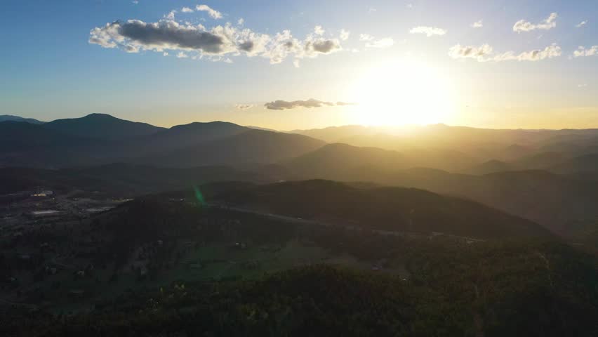 Summer sunrise over Golden, Colorado, golden light spilling across foothills, Clear Creek shining, and vehicles moving along curving roads toward the mountains.