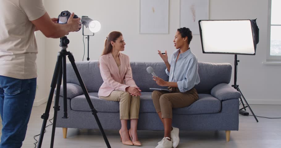 African American reporter conducts interview with guest for tv show, cameraman recording video on camera, engaging in news conversation, communication, talk for broadcast in a lively setting.
