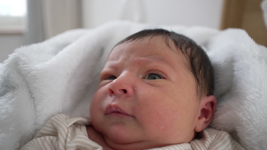 Newborn baby lying on a soft blanket, with a focused, peaceful expression. baby's delicate features, capturing a serene moment of early life