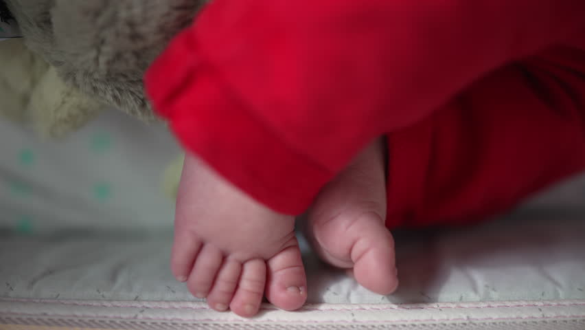 Close-up of tiny newborn feet in red pants, showcasing delicate toes and soft skin, highlighting the innocence and tenderness of a newborn in a precious and fragile moment