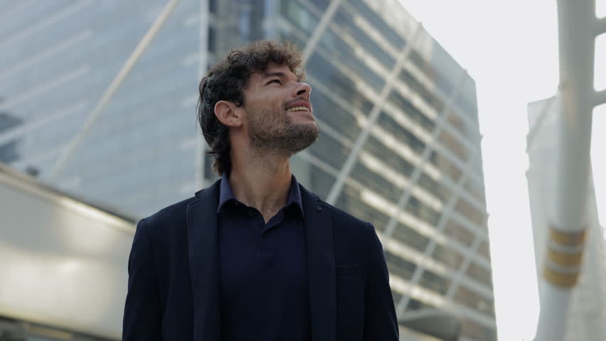Portrait of Hispanic man office employee smiles and looks upward in urban landscape. Ambitious Latin man entrepreneur dreams about success on downtown street. Big career plans