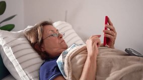 Elderly woman relaxing in bed while using a red smartphone, showcasing modern technology usage by seniors and a peaceful home environment - Powered by Shutterstock - Get 15% off with code: PIKWIZARD15