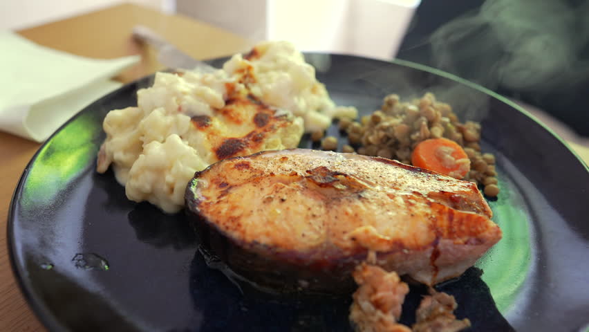 Grilled salmon steak served with creamy mashed potatoes and a side of sautéed lentils with carrots, showcasing a balanced and nutritious meal presentation