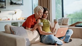 Lesbian girls looking computer at modern living room. Domestic women cuddling sofa drinking coffee shopping online on laptop. Happy young couple ordering stuff in e-commerce store embracing in flat - Powered by Shutterstock - Get 15% off with code: PIKWIZARD15