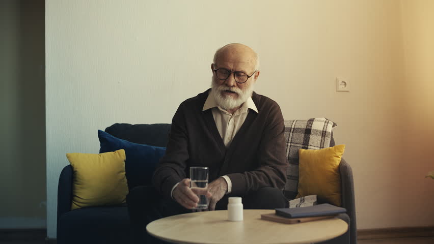 Elderly bearded man taking vitamins with water, healthy lifestyle in old age