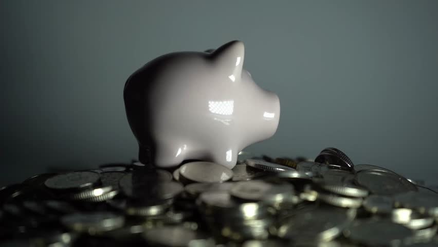 Piggy bank standing on pile of coins against white background, symbolizing economy, savings, investment, financial growth, and wealth management concept.