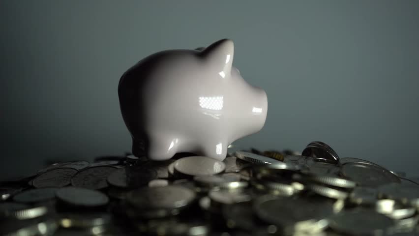 Piggy bank standing on pile of coins against white background, symbolizing economy, savings, investment, financial growth, and wealth management concept.