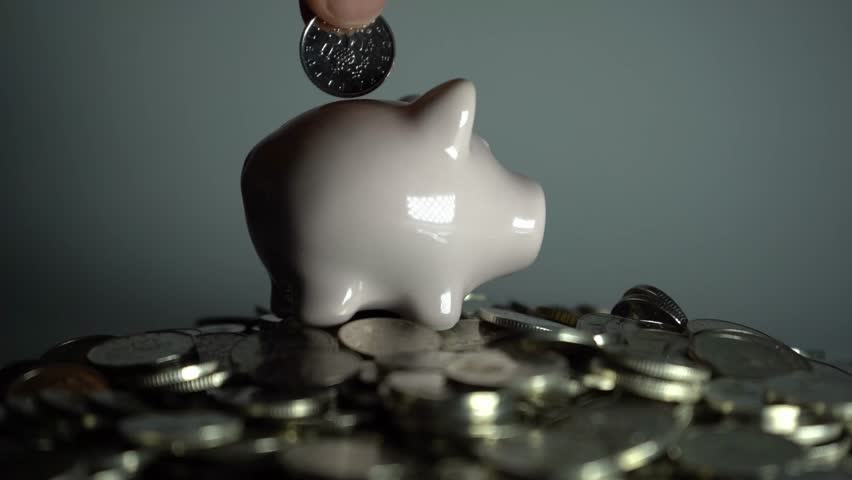 Piggy bank standing on pile of coins against white background, symbolizing economy, savings, investment, financial growth, and wealth management concept.
