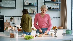 Happy friends cooking together inside sunny kitchen morning light closeup. Cheerful ladies watching culinary show on tablet making breakfast at home. Active woman slicing veggies talking to roommate - Powered by Shutterstock - Get 15% off with code: PIKWIZARD15