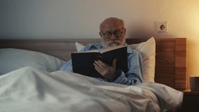 Senior man reading a book while lying in bed, enjoying hobby in calm retirement - Powered by Shutterstock - Get 15% off with code: PIKWIZARD15