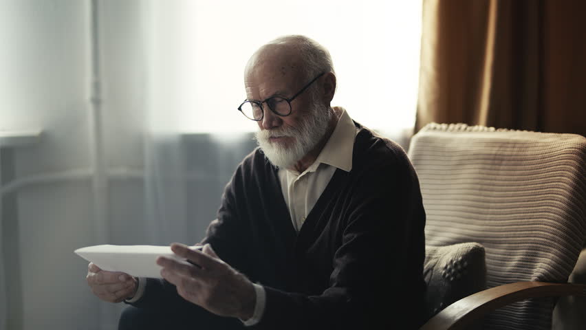 Lonely elderly man reading energy bill letter, shocked by high utility costs